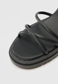Sandales noires à lanières avec une finition en cuir mat et lisse. Elles disposent d'une semelle épaisse et coussinée et de plusieurs lanières entrecroisées pour un bon maintien.
