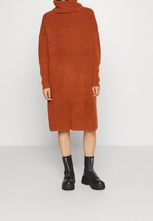 Person wearing a knee-length burnt orange turtleneck sweater dress and black chunky mid-calf zip boots, standing on a plain background.