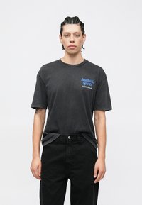 Pelēka kokvilnas T-krekls ar priekšpusē zilā krāsā rakstītu uzrakstu “Southside Spirits Chicago”. Kombinēts ar melnām biksēm, radot ikdienišķu izskatu.