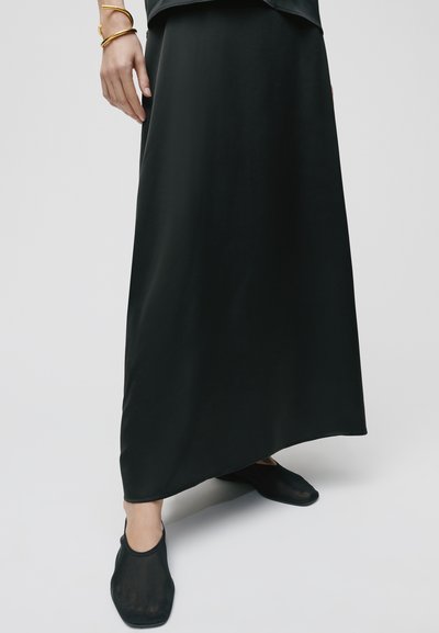 Fekete maxi szoknya sima anyagból, egyenes szabású dizájnnal. Fekete, félátlátszó slip-on cipővel párosítva.