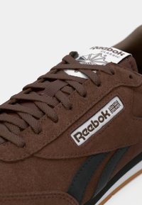 Brahma zamšs sporta apavi ar melniem akcentiem, ar biezām auklām un baltu logotipa mēli. Strukturēta virsma un klasiskie dizaina elementi.