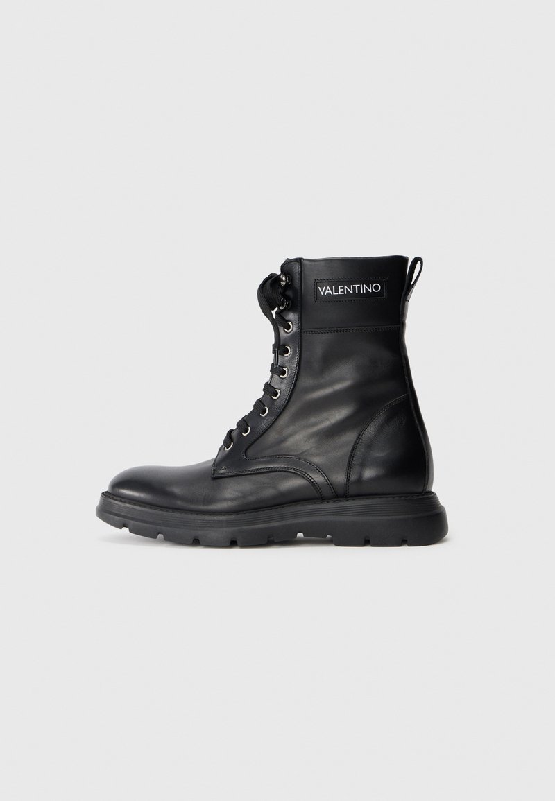 Bottine en cuir noir avec un bout rond, devant à lacets, col rembourré, semelle épaisse et étiquette de marque avec "VALENTINO" sur le côté.
