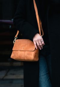 Brown leather shoulder bag with a flap closure, adjustable strap, and gold hardware. Smooth texture with a minimalist design.