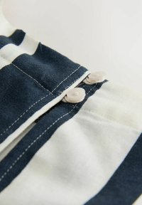 Pruhovaná látka v námořnickém modrém a bílé barvě, se plastovými knoflíky a kontrastním šitím podél okraje. Měkká, texturovaná směs bavlny.