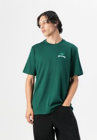 Zöld pamut póló rövid ujjakkal és kerek nyakkivágással, bal mellrészen fehér Adidas logó található. Fekete nadrág.
