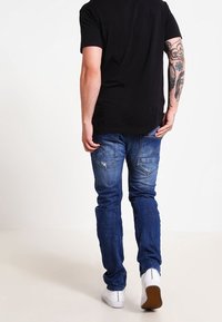 Blå denimjeans med en urtvättad finish, femfickorsdesign och subtil slitage. Parat med en svart t-shirt och vita sneakers.