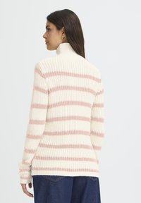 Suéter de cuello alto a rayas en crema y rosa claro. Textura de punto, mangas largas y puños acanalados. El dobladillo se sitúa a la altura de la cadera con pequeñas aberturas laterales.