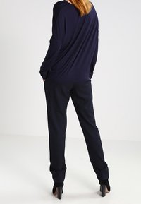 Haut ample bleu marine avec dos drapé et manches longues, associé à un pantalon bleu marine assorti, porté avec des chaussures noires à talons.