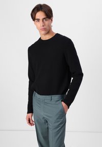Jersey negro con cuello redondo, combinado con pantalones elegantes de color azul claro. La tela parece suave y presenta una silueta ajustada.