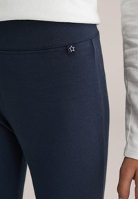 Tengerészkék leggings puha anyagból, sima tapintású felülettel és egy kis csillag logóval ellátott címkével a derékrészen.