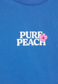 Tissu bleu avec texte blanc « PURE PEACH » et un graphique de fleur rose recouvrant la lettre H dans « PEACH ».