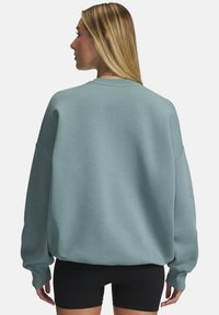 Lichtblauwe oversized sweatshirt met ribgebreide manchetten, ronde hals en zachte textuur, getoond vanaf de achterkant tegen een effen achtergrond.