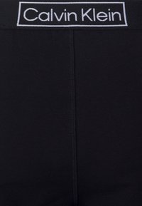Fekete boxer alsónadrág puha, rugalmas derékpánttal, fehér hímzett "Calvin Klein" logóval, sima anyagból készült és varrás nélküli kialakítással.