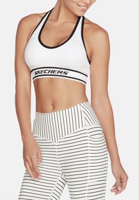 Sujetador deportivo blanco con ribete negro y el logo de "SKECHERS". Combinado con leggings de cintura alta a rayas blancas y negras con una textura suave.