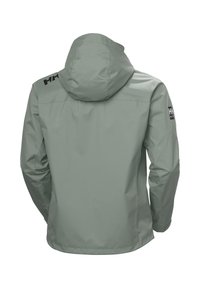 Chaqueta impermeable verde claro con capucha, que presenta una textura suave, puños ajustables y acentos de logo negro en el hombro.