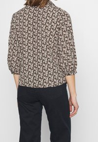 Blusa floreale in marrone scuro con motivi rosa e bianchi; presenta un colletto e maniche a tre quarti, vestibilità cropped con una leggera texture.