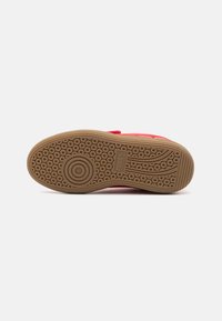Rød sneaker med teksturert overdel, gummisåle med sirkulære og bølgende mønstre, og en logo preget på siden.