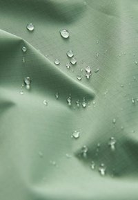 Wasserabweisender grüner Stoff mit einer Rautenmuster-Oberfläche, auf der Wassertropfen liegenbleiben und die wasserdichten Eigenschaften zeigen.