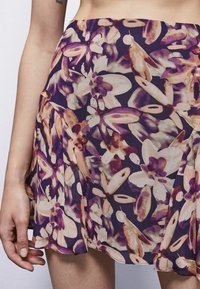 Gonna con motivo floreale in una combinazione di colori viola e crema, realizzata in tessuto leggero. Presenta delle pieghe e una consistenza morbida e fluida.