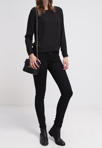 Svart långärmad topp tillsammans med svarta skinny jeans och ankelskor. En liten svart handväska med kedjesnor fulländar outfitten.