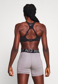 Svart sport-bh med justerbara axelremmar och hängslen, parat med ljusgrå shorts som har en svart midjeband med logotypdetalj.