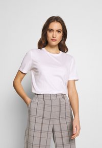 Weißes kurzärmliges T-Shirt mit Rundhalsausschnitt, kombiniert mit hellgrauen karierten Hosen, die blaue und braune Streifen aufweisen.