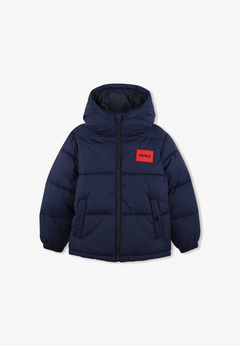 Veste matelassée bleu marine avec capuche, fermeture éclair frontale, deux poches à boutons-pression et un patch rectangulaire rouge marqué HUGO sur la poitrine.