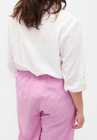 Camicia di lino bianca con maniche arrotolate, abbinata a pantaloni larghi di un rosa chiaro. Presenta un tessuto morbido e testurizzato e una cintura elastica.