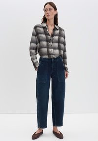 Overhemd met knopen in een zwart-wit ruitpatroon, gecombineerd met hoge donkere denimbroek met voorzakken en een losse pasvorm.