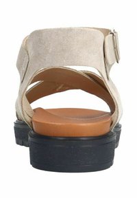 Beige suède sandaal met een open achterkant, een bruine voetbed en een zwarte gemarmerde zool. Verstelbare enkelband met metalen gesp detail.