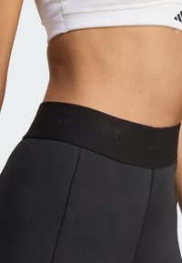 Leggings sportivi neri con una larga vita nera che presenta il marchio "TECHFIT" in rilievo. Texture liscia e design aderente.