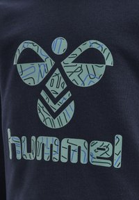 Marinblått tyg har en grön grafik med ett symmetriskt mönster och mönstrade accenter som visar ordet "hummel" i liknande stil.