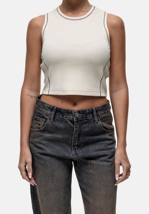 Donna che indossa un top corto bianco senza maniche con cuciture nere e jeans neri sbiaditi a vita alta, mostrata dalle spalle ai fianchi.