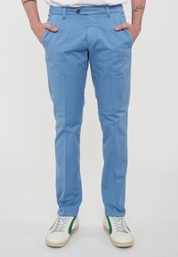 Chino in cotone azzurro chiaro con taglio slim, dotati di tasche laterali, chiusura con bottone e abbinati a sneaker bianche con dettagli verdi.
