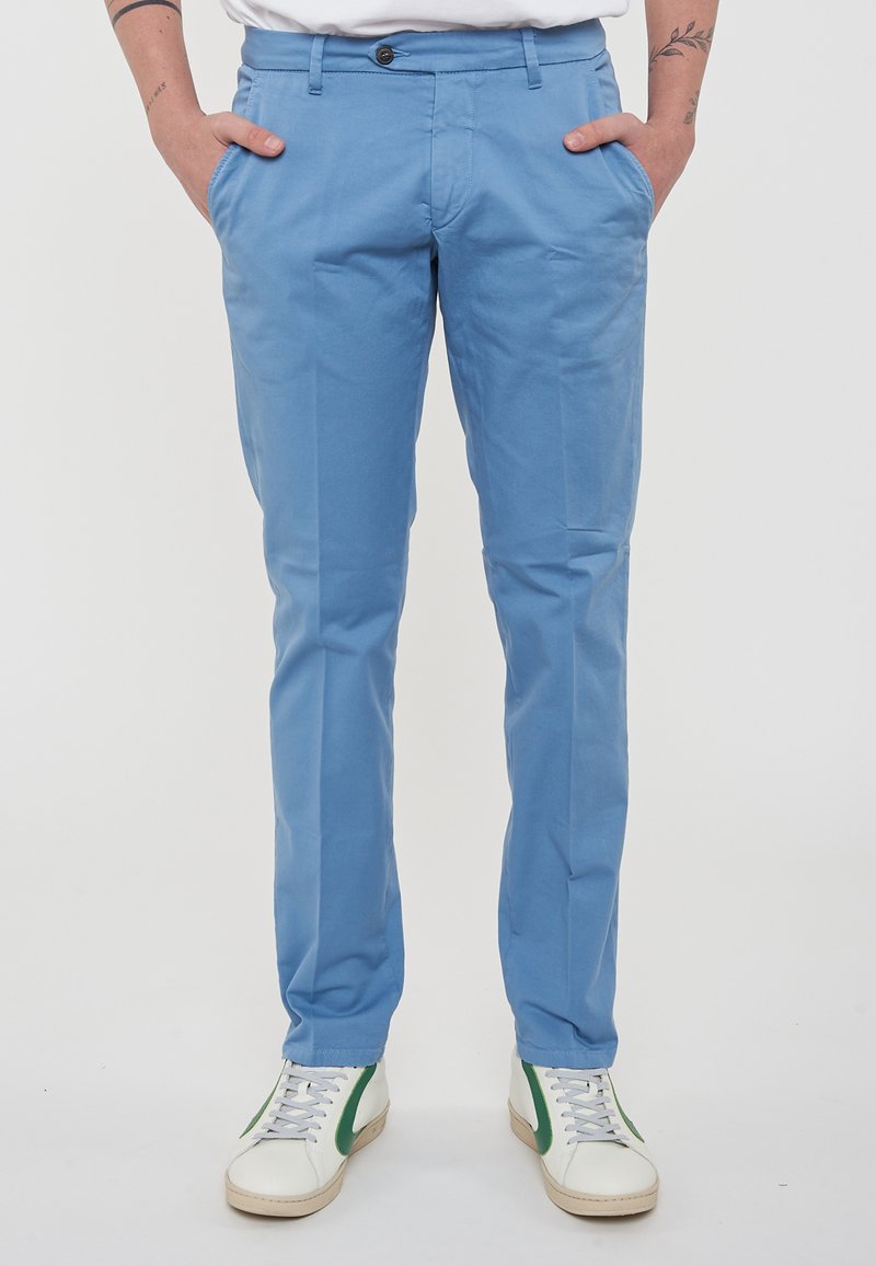 Chino in cotone azzurro chiaro con taglio slim, dotati di tasche laterali, chiusura con bottone e abbinati a sneaker bianche con dettagli verdi.
