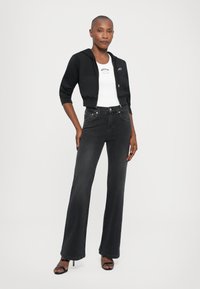 Felpa nera corta con zip, top aderente bianco e jeans neri a vita alta a campana. Indossati con tacchi neri con cinturini.