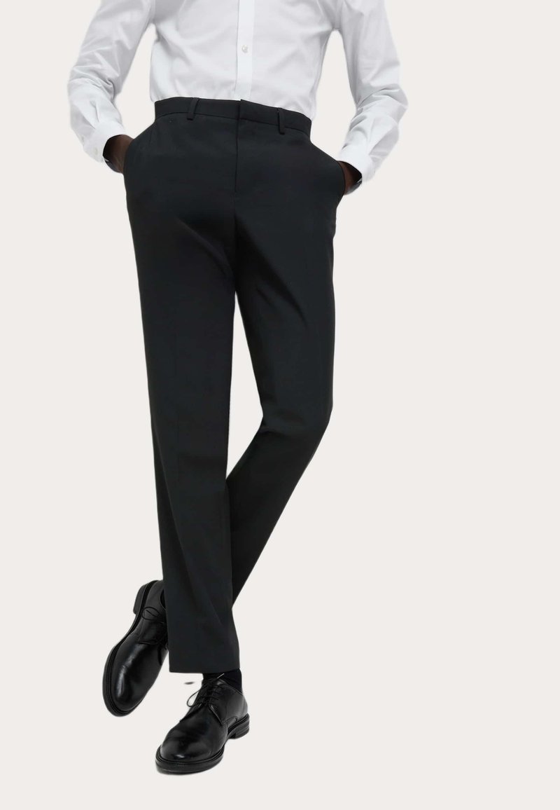 Czarne spodnie garniturowe o dopasowanym kroju, wykonane z gładkiego materiału, z bocznymi kieszeniami i prostym przodem, w połączeniu z czarnymi skórzanymi butami.