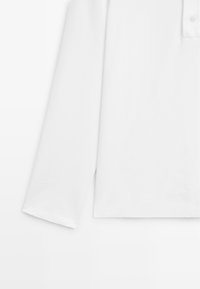 Langärmliges weißes Poloshirt mit gerippten Bündchen und einer Knopfleiste mit zwei Knöpfen auf einem schlichten Hintergrund.