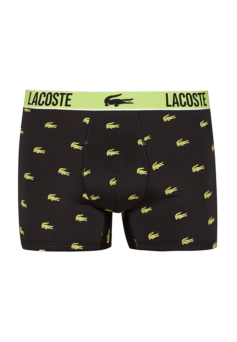 Czarne bokserki z zielonym paskiem, na którym widnieje napis "LACOSTE". Materiał pokryty jest powtarzającymi się żółtymi logo krokodyla.