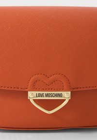 Orange textured handbag flap with gold heart-shaped clasp engraved with "LOVE MOSCHINO" logo.