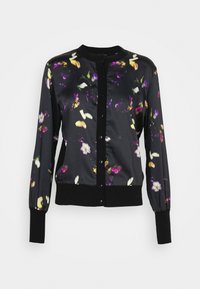 Blouse noire à manches longues boutonnée, avec poignets et ourlet côtelés, présentant des motifs floraux violets, jaunes et blancs dispersés.