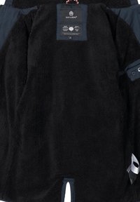 Black fleece jacket featuring a soft, textured surface, side openings, and a label detailing brand information at the neckline.
