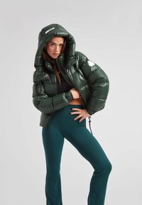 Grønne puffjakke med hætte, der har en blank finish, lynlåsfront og elastiske manchetter. Parret med tætsiddende grønne leggings.