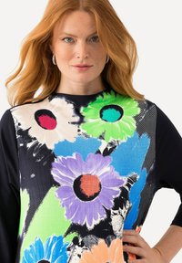 Lockere Bluse mit kräftigen, mehrfarbigen Blumenmustern auf einem strukturierten, leichten Stoff, schwarzen Ärmeln und einem runden Halsausschnitt.
