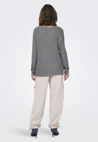 Grauer Strickpullover mit weitem Ausschnitt und langen Ärmeln, kombiniert mit hellbeigen Cargo-Hosen. Das Outfit zeichnet sich durch einen lockeren Sitz und strukturierten Stoff aus.