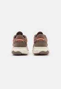 Brown sneakers with a textured fabric upper, orange accents, and a chunky cream rubber sole. Features a padded collar and lace closures.