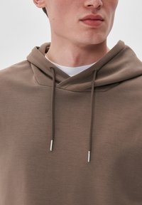 Sudadera marrón con cuello cruzado, de color claro por debajo y cordones con puntas metálicas. Textura suave con detalles de diseño mínimos.