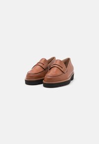 Tan leather loafers with a rounded toe, decorative strap across the upper, and a thick black outsole with tread patterns.