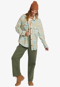 Plaid flannel shirt in light blue and beige, featuring two chest pockets, button closure, paired with olive green pants and tan boots.