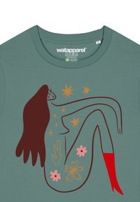 T-shirt en coton vert orné d'un graphique stylisé représentant une figure avec des cheveux bruns, des bottes rouges et des accents floraux en rose et en or.
